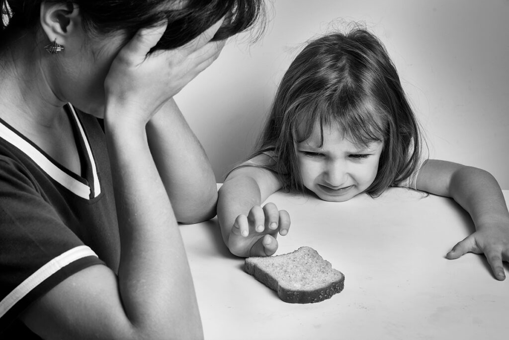A depressed mother and a hungry daughter pulling her hand to a piece of bread.
